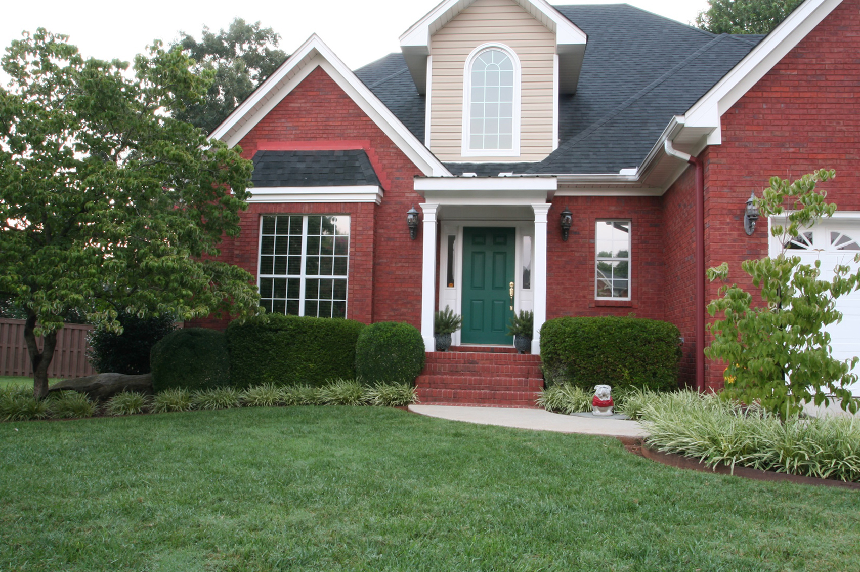 A red brick home with a green front door and white trim